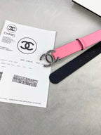 Chanel belt with pink strap and large CC medallion buckle resting on black backing.