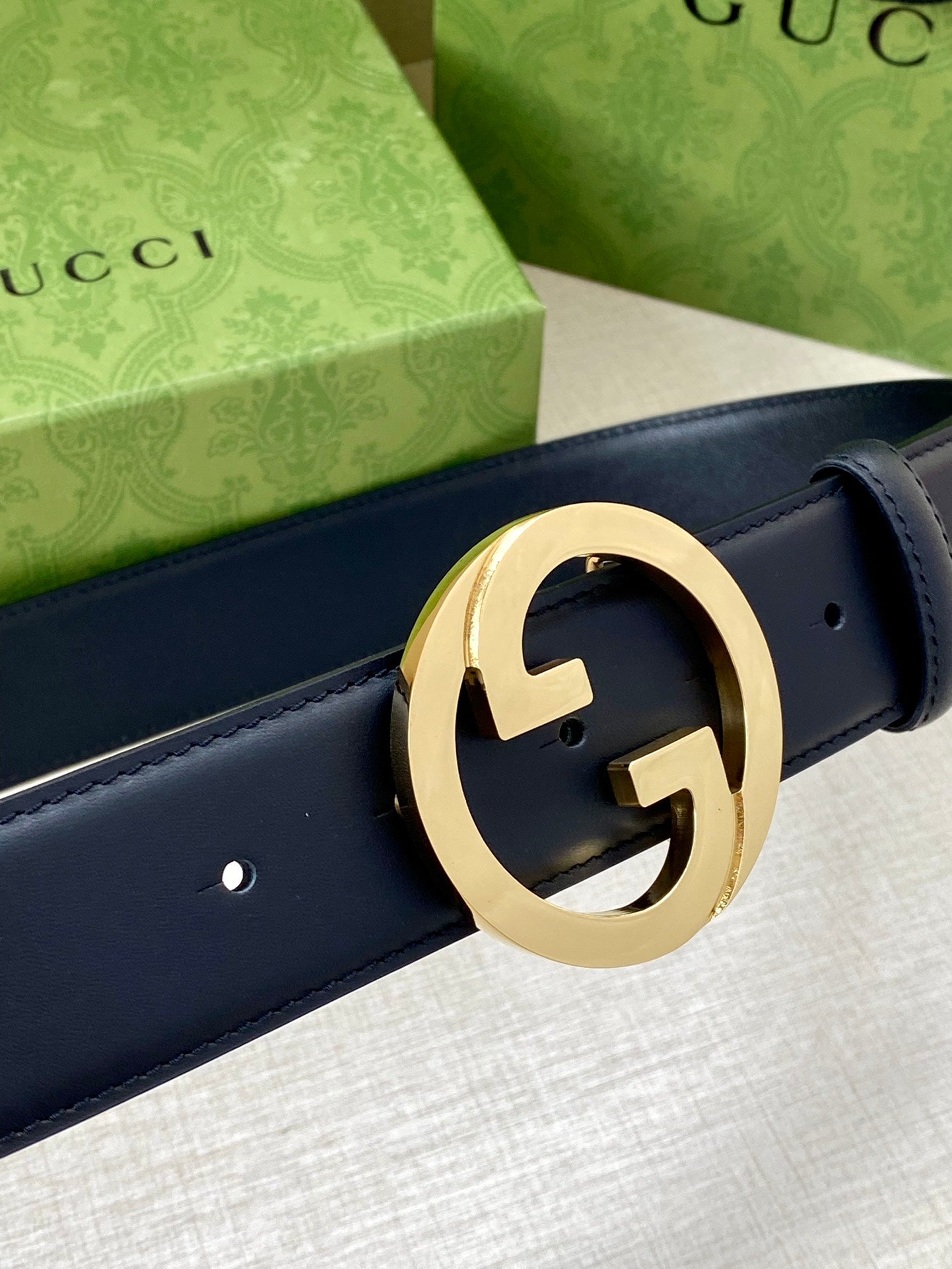Dark blue leather belt detail with gold-tone GG buckle and visible punch holes