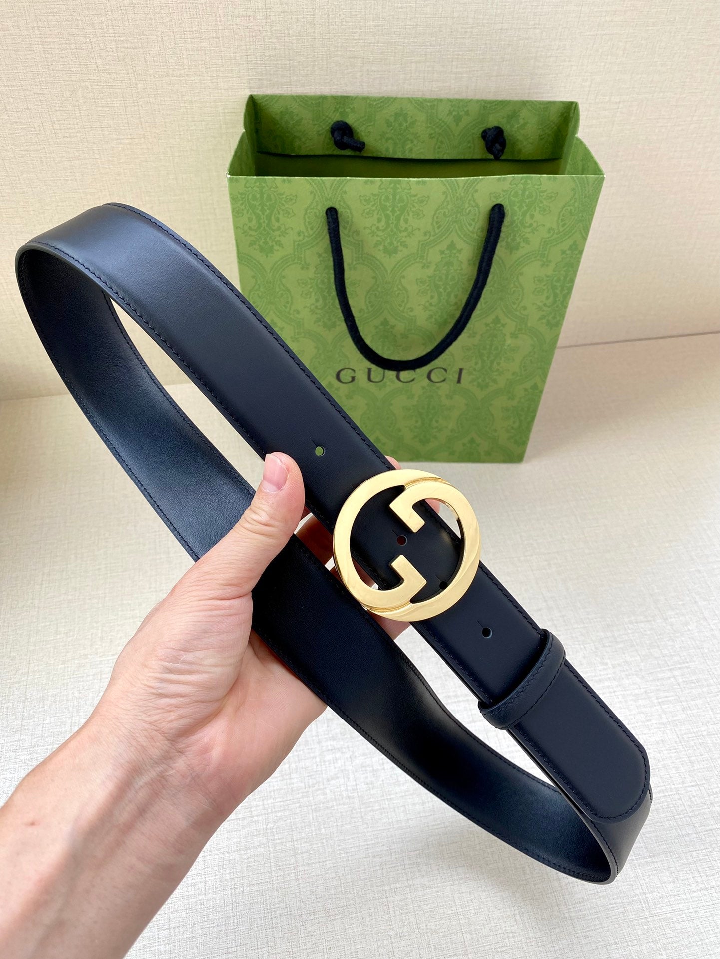 Navy leather belt laid flat with gold GG buckle and stitched double-strap edge
