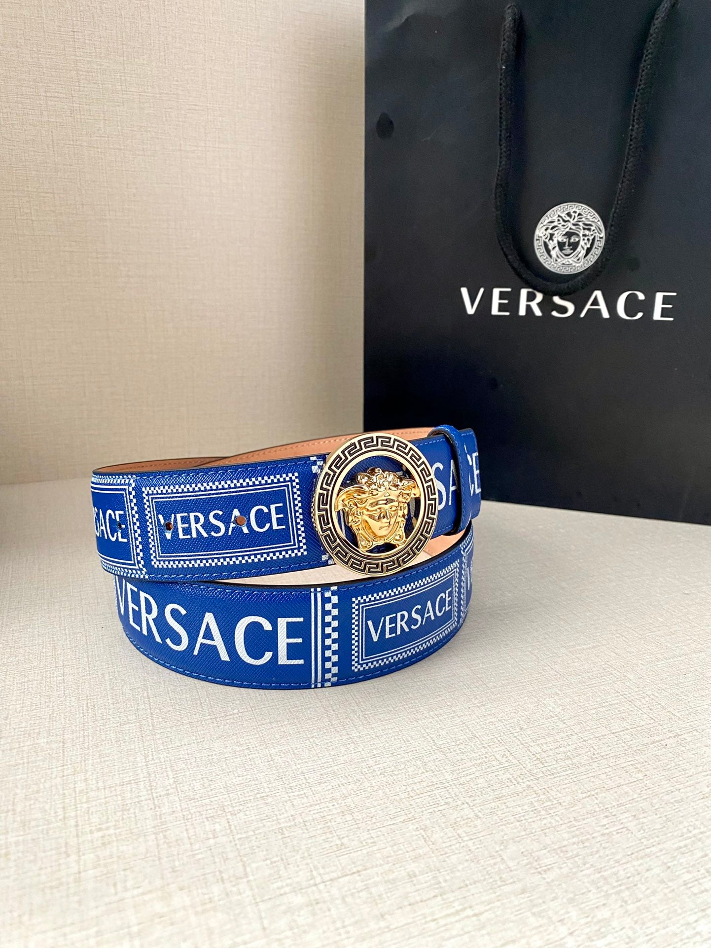 Versace belt on table: blue webbing strap with gold-tone round medallion buckle
