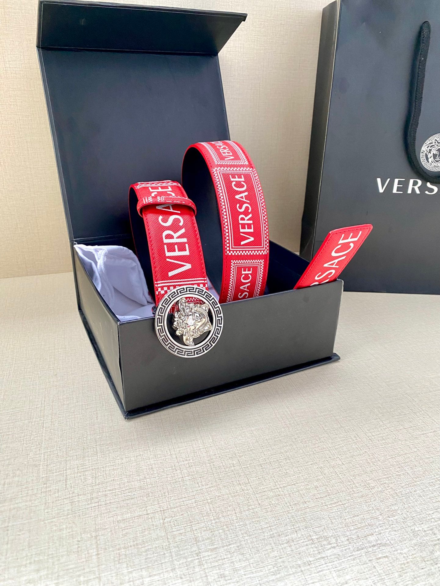 Versace belt with red logo strap and circular lion buckle in open box