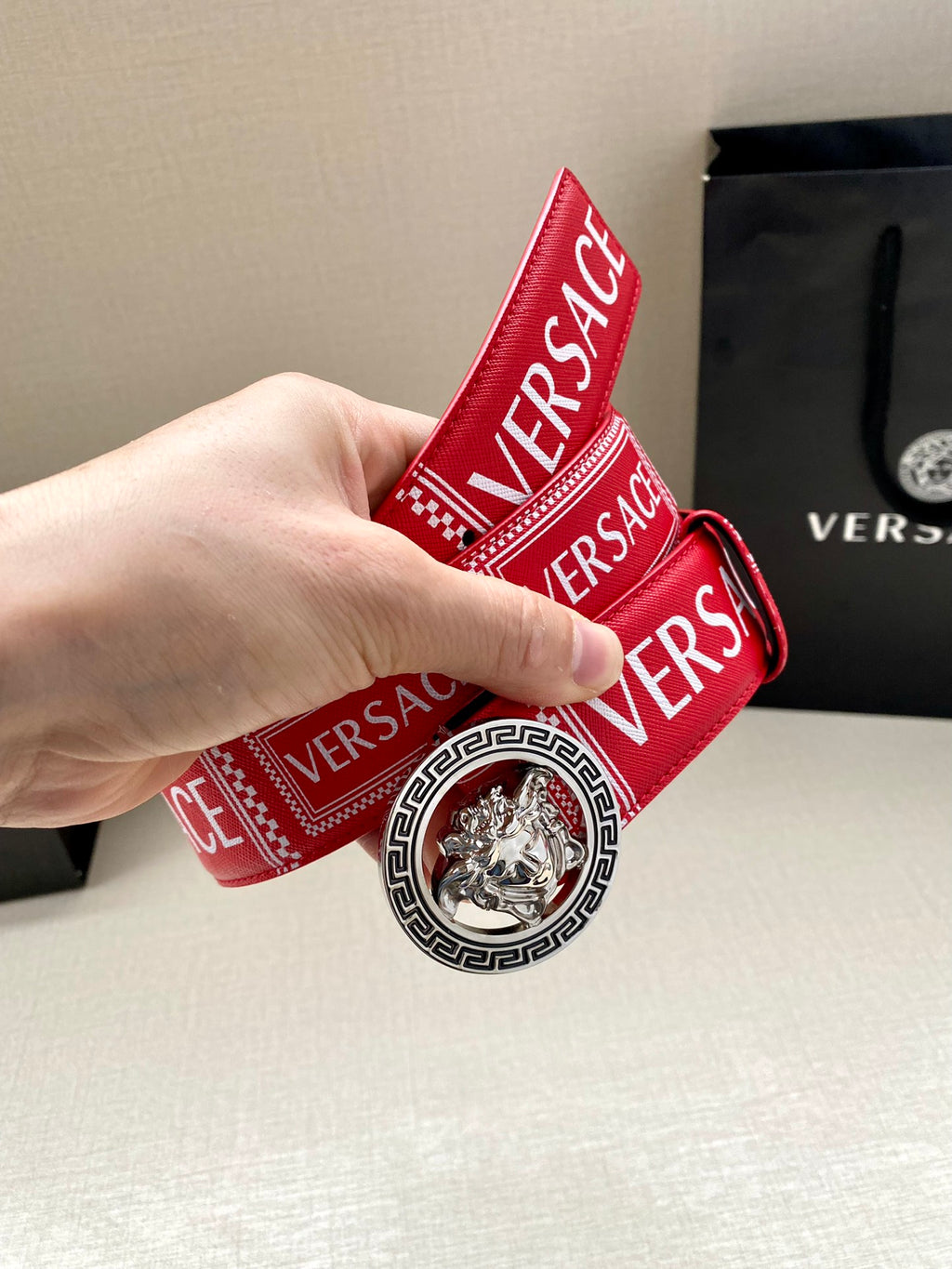 Versace belt held upright, red logo strap with circular lion buckle