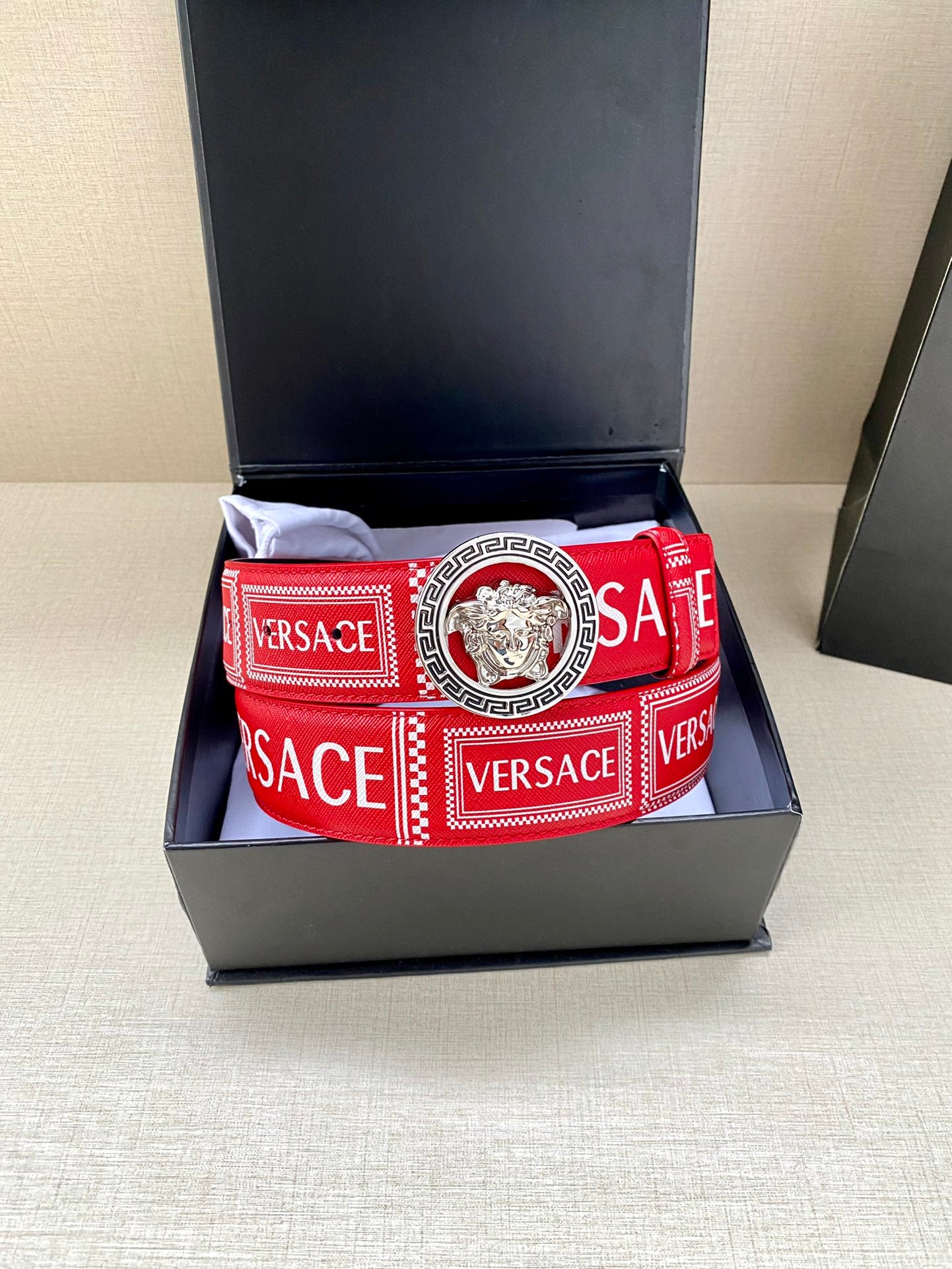 Versace belt in open box on cushion, red logo strap with lion buckle