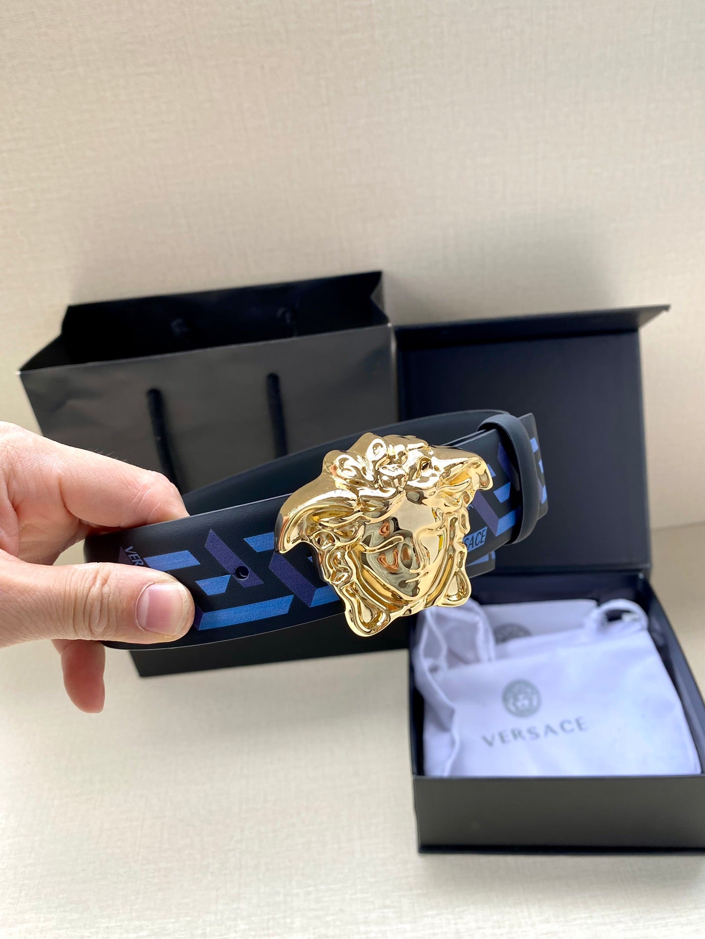 Designer belt with blue patterned strap and gold lion buckle in gift packaging
