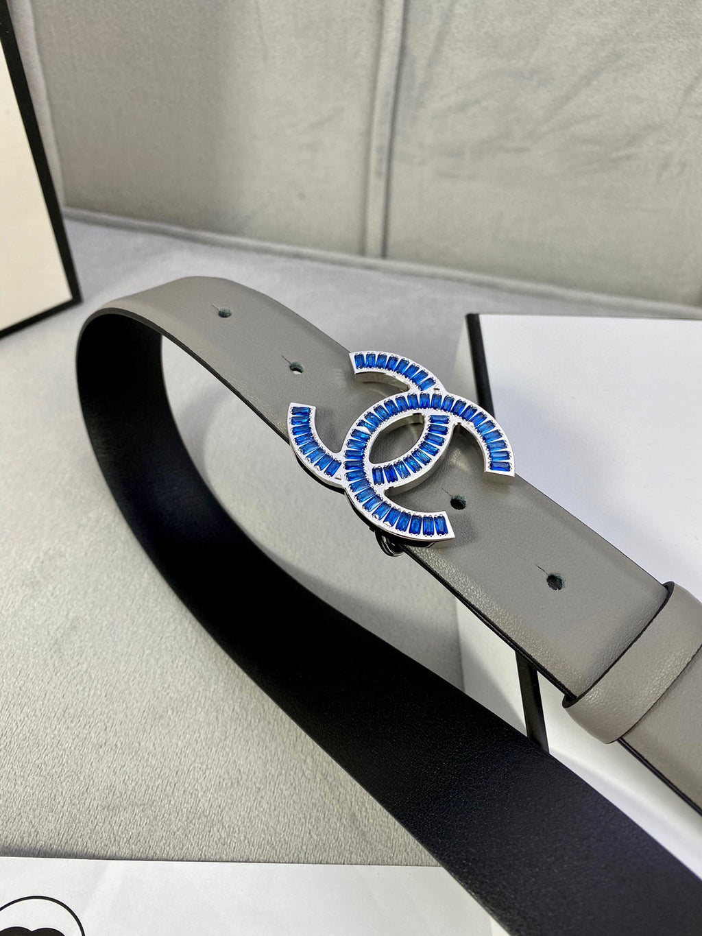 Chanel belt in light gray leather with blue-and-gold logo buckle and black inner lining