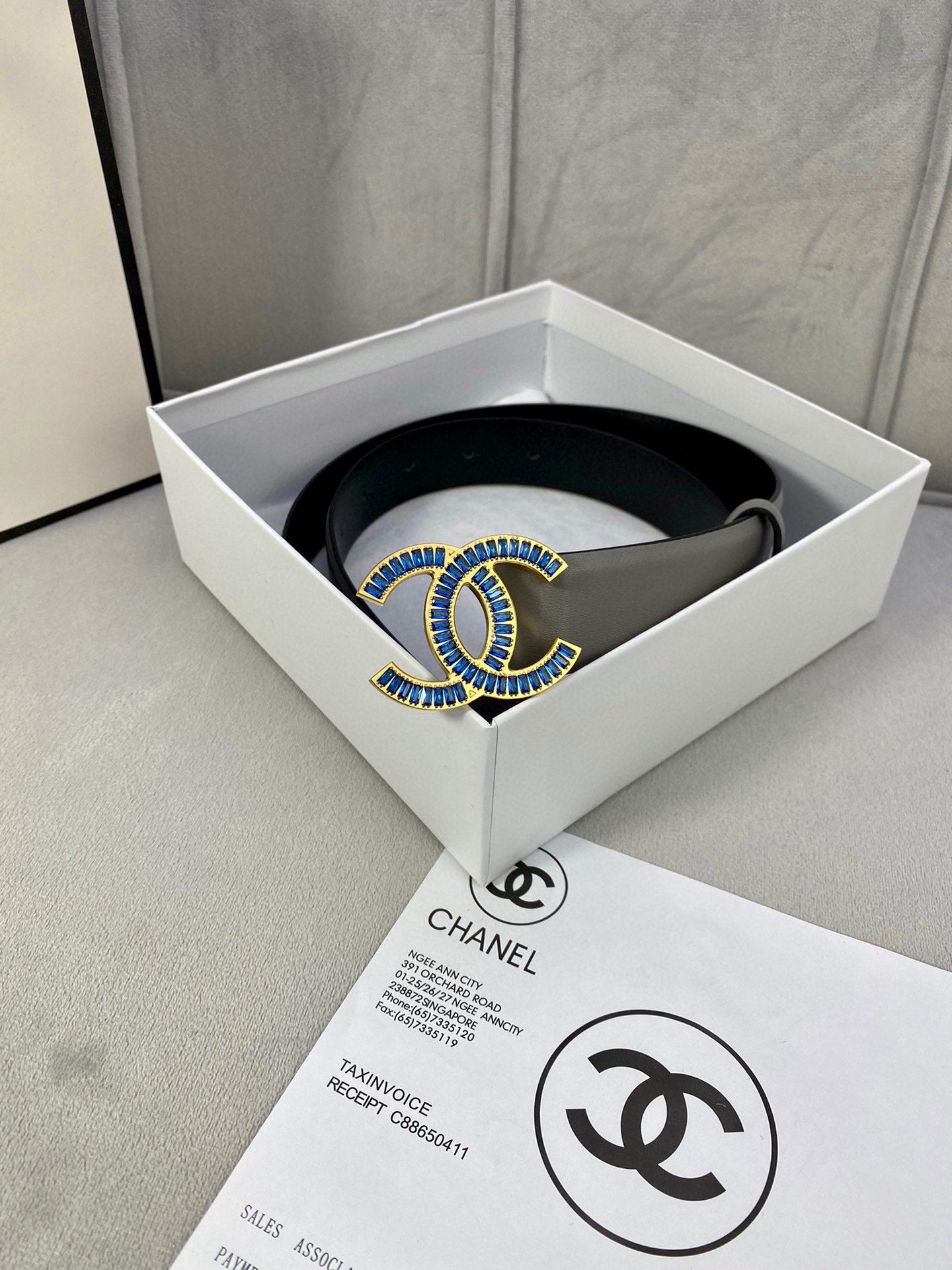 Chanel belt in light gray leather with blue-and-gold logo buckle, flat view