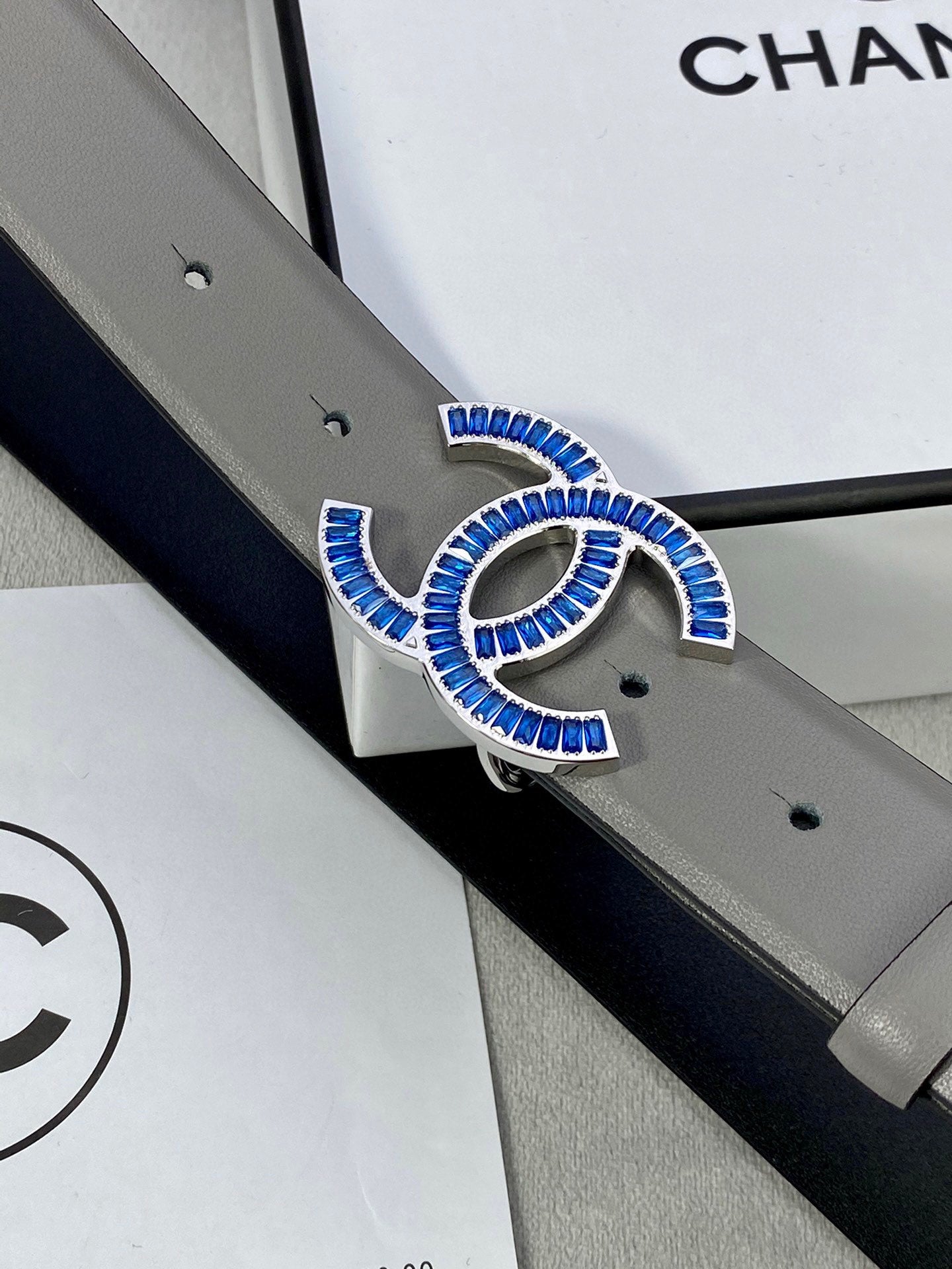 Chanel belt close-up: blue-and-gold logo buckle on light gray leather strap