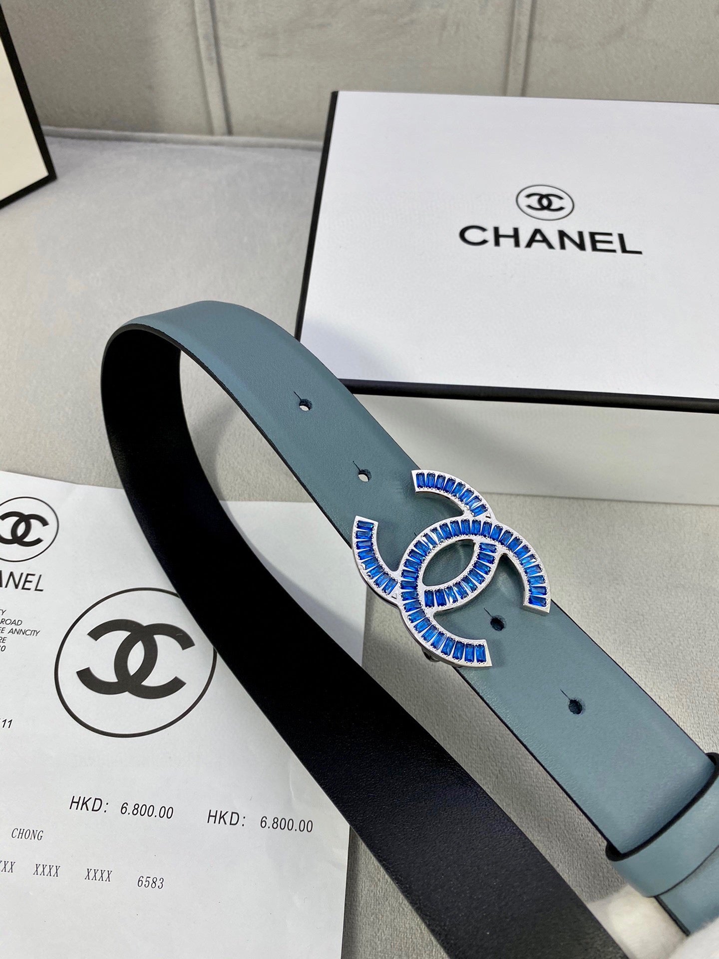 Light blue Chanel belt with blue and gold logo buckle on strap, angled close-up