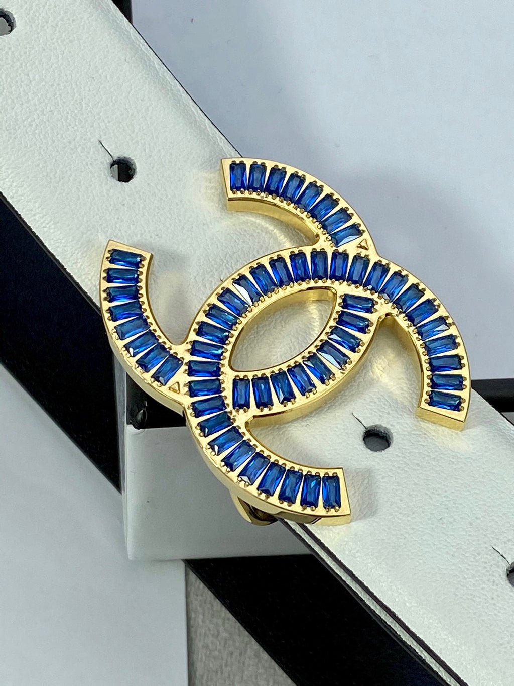 White belt strap with gold-and-blue CHANEL logo buckle close-up