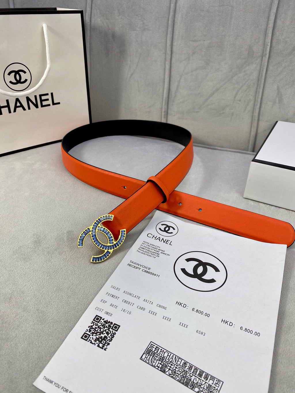 Chanel orange leather belt with blue CC buckle, laid over packaging card