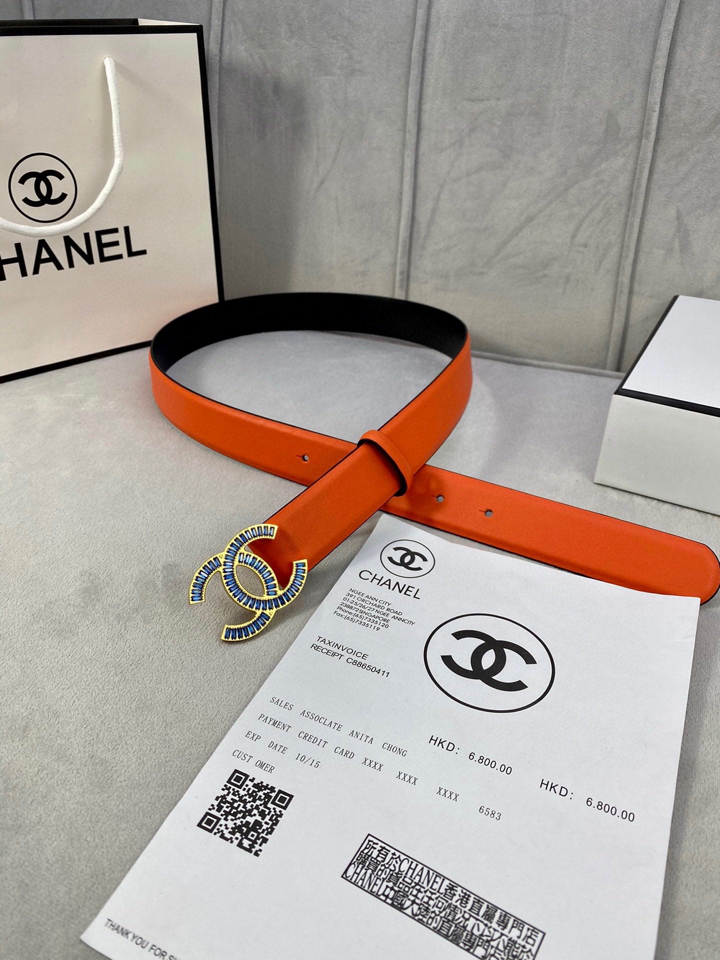 Chanel orange leather belt with blue CC buckle, laid over packaging card