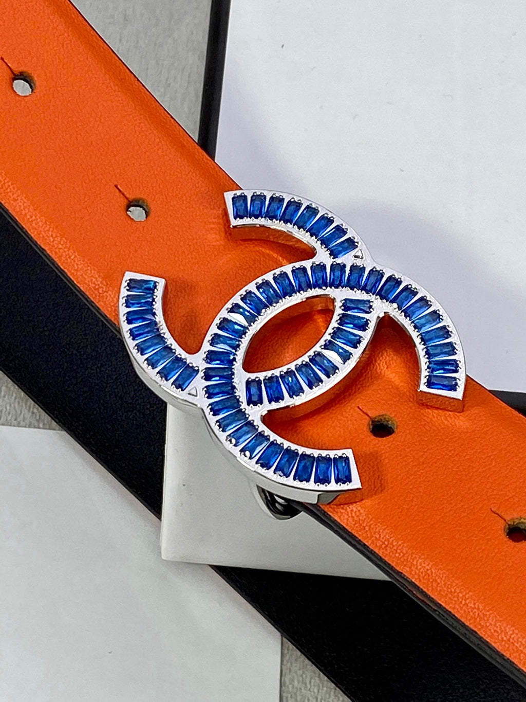Chanel belt buckle close-up: blue CC logo on orange leather strap