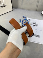 Tan leather belt held in hand, multicolor jeweled logo buckle visible