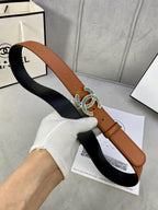 Tan leather belt with dark backing and multicolor logo buckle, shown in hand