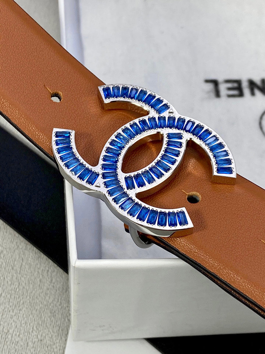 Close-up of tan belt with multicolor jeweled logo buckle and punched holes