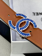 Close-up of tan belt with multicolor jeweled logo buckle and punched holes