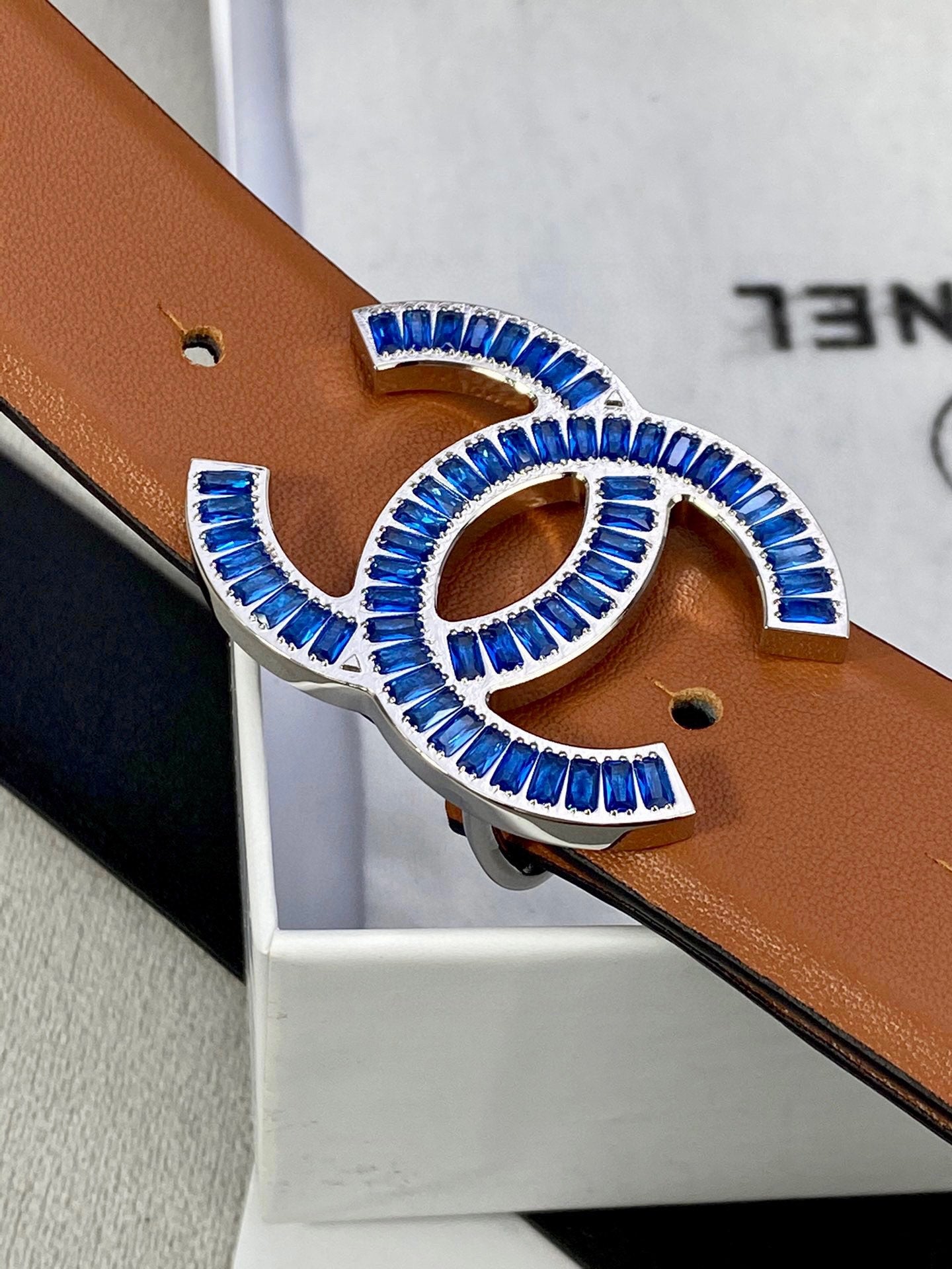 Close-up of tan belt with multicolor jeweled logo buckle and punched holes