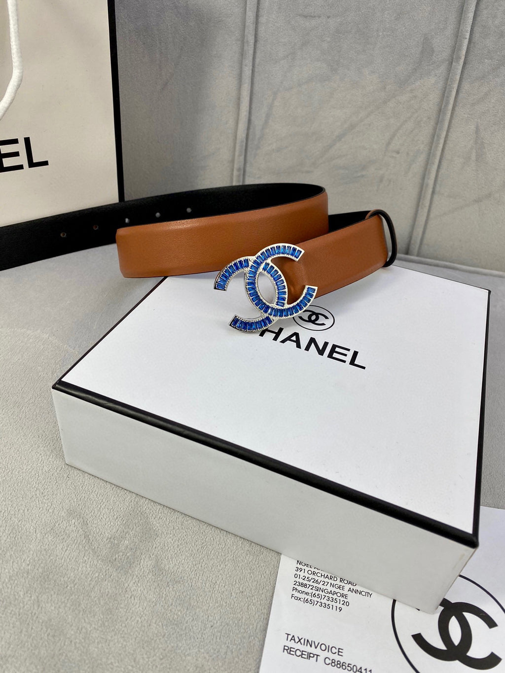 Tan leather belt with multicolor logo buckle resting on white box