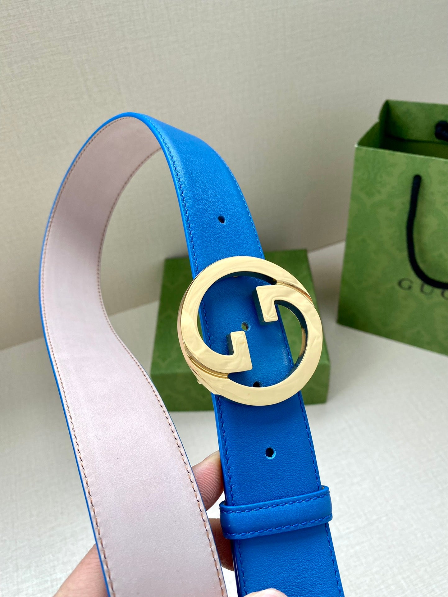 Blue Gucci belt with gold-tone GG buckle in round frame, beige lining and edge stitching.