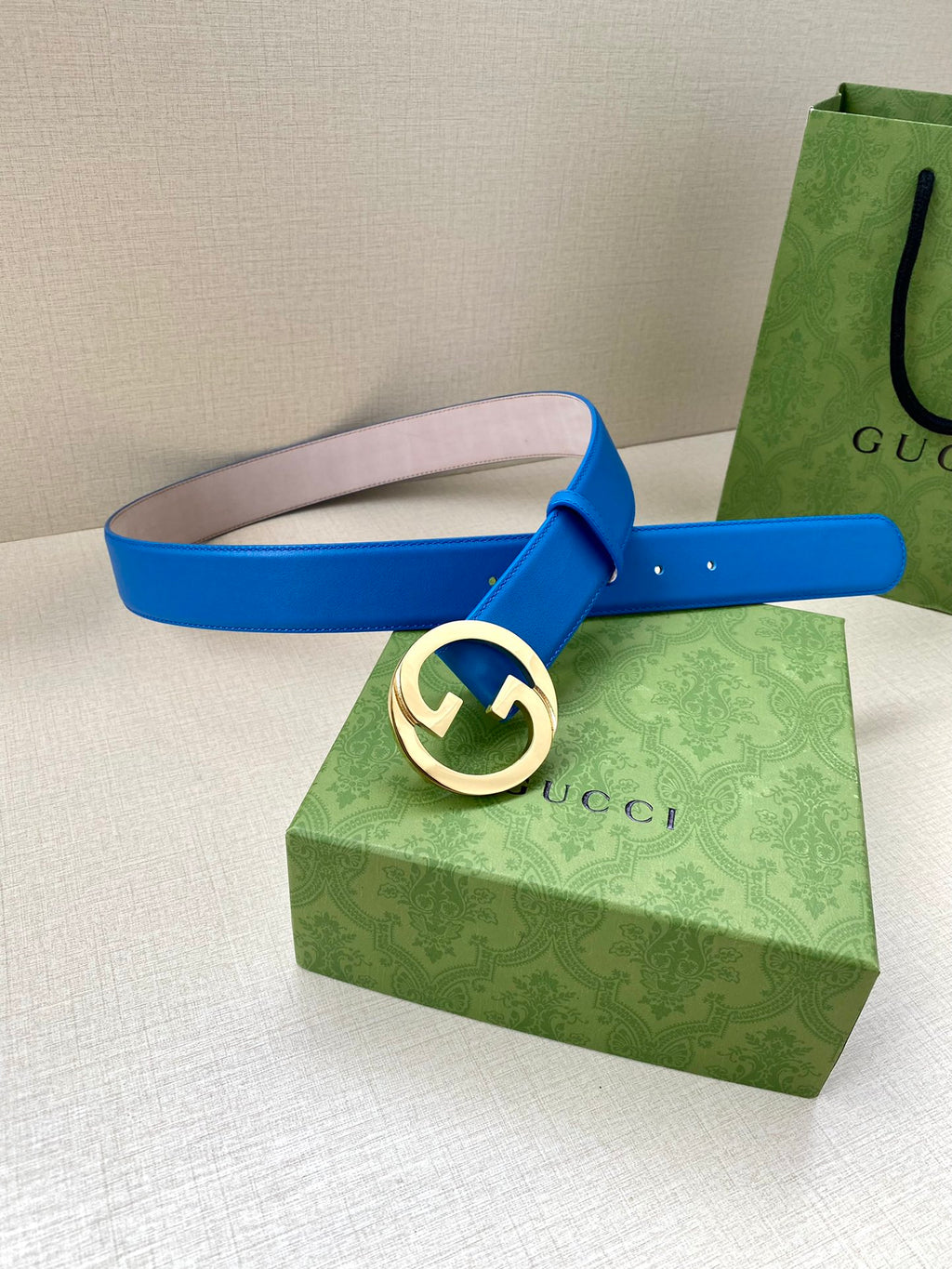 Blue Gucci belt with large round GG buckle, laid flat, pin holes visible.