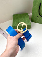 Blue Gucci belt with gold-tone GG buckle in round bezel, strap end and pin holes visible.