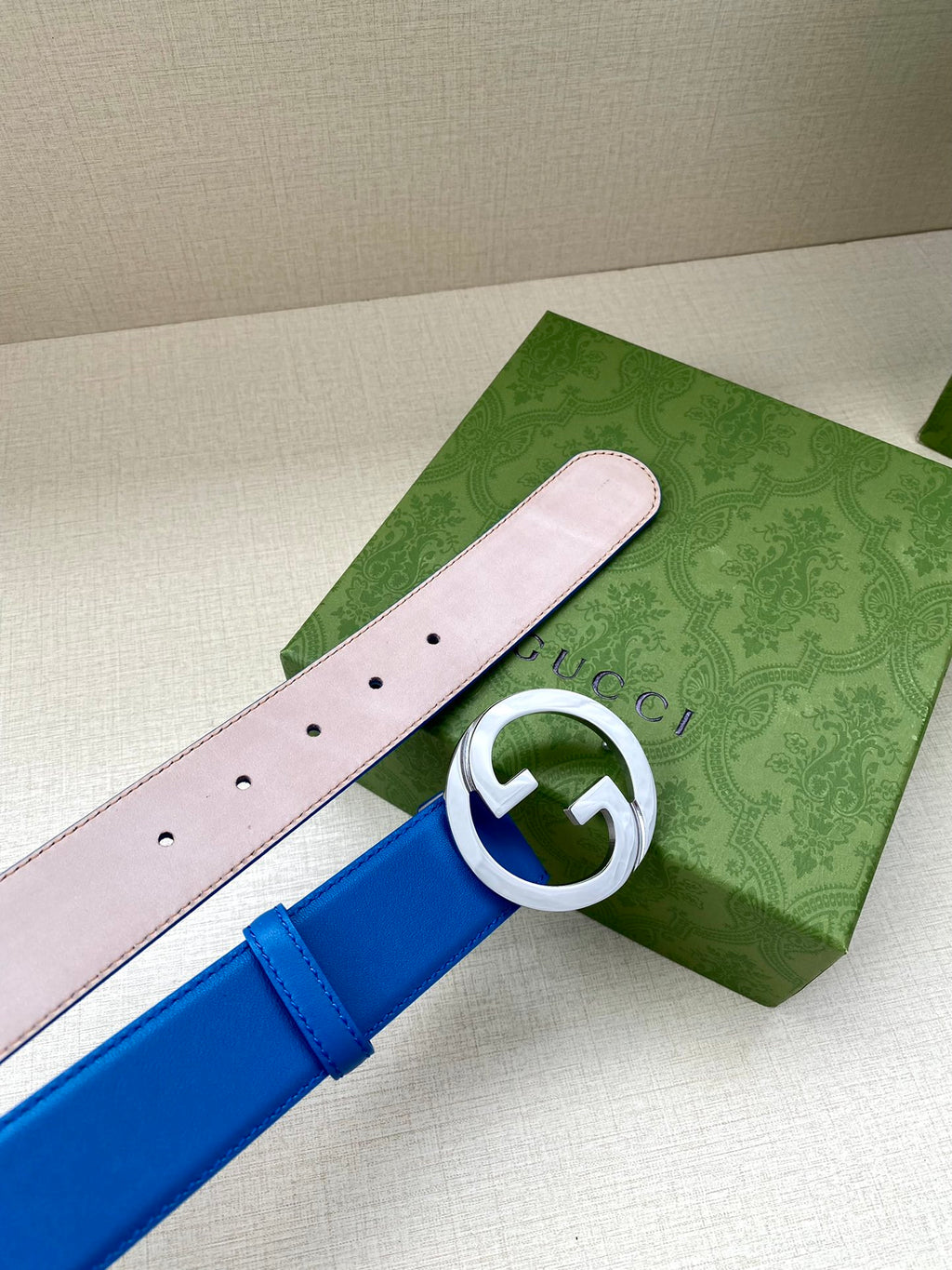 Blue Gucci belt with silver-tone GG buckle, pale pink reverse strap with pin holes.