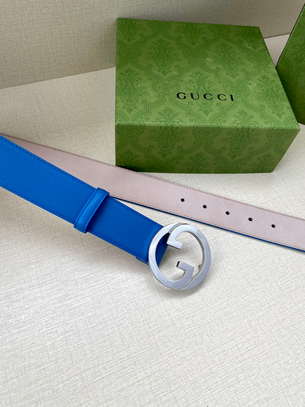 Blue Gucci belt with silver-tone round GG buckle, pale pink strap end with holes.