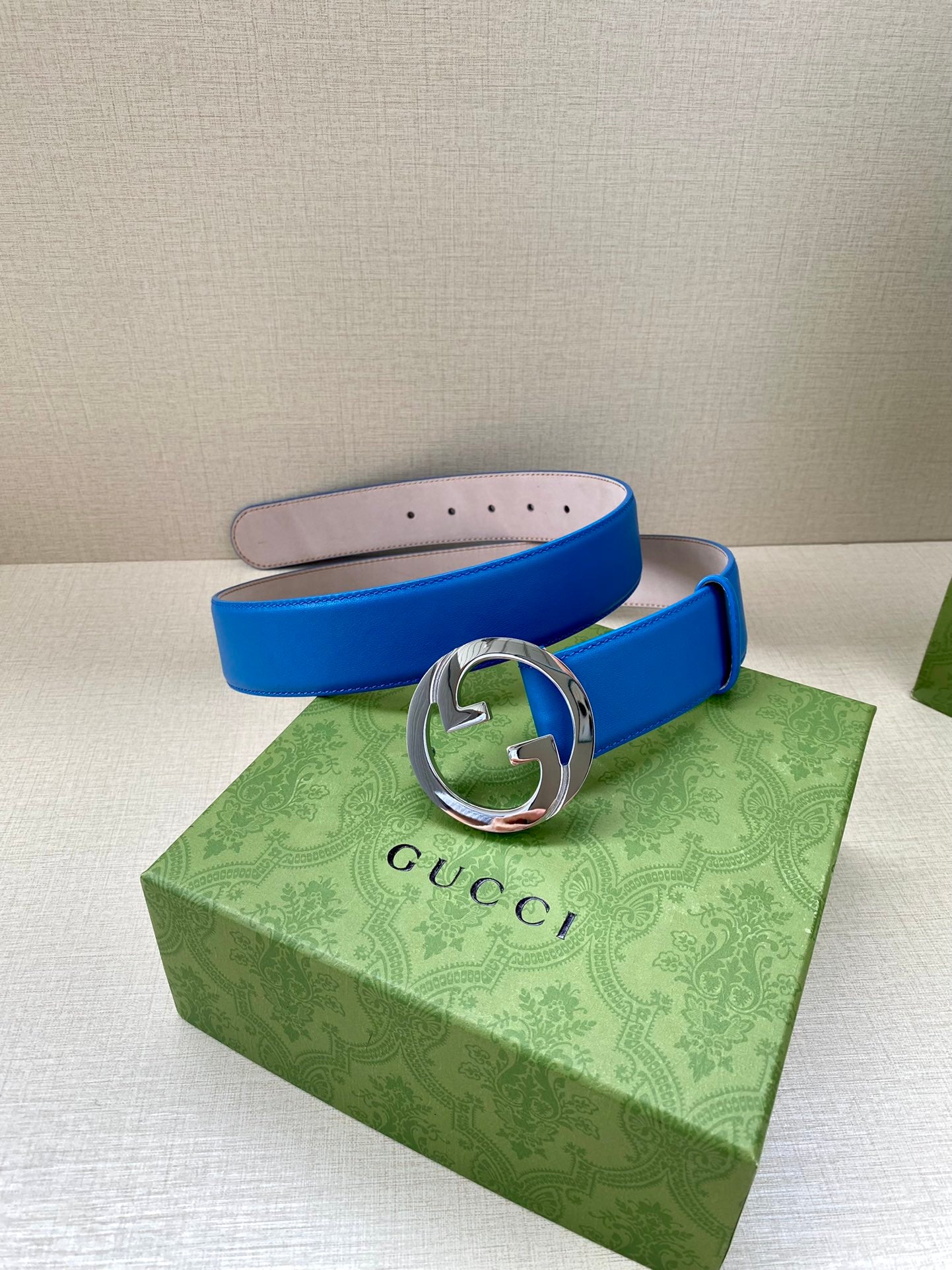 Blue Gucci belt with silver-tone GG buckle, belt end and perforated strap holes visible.