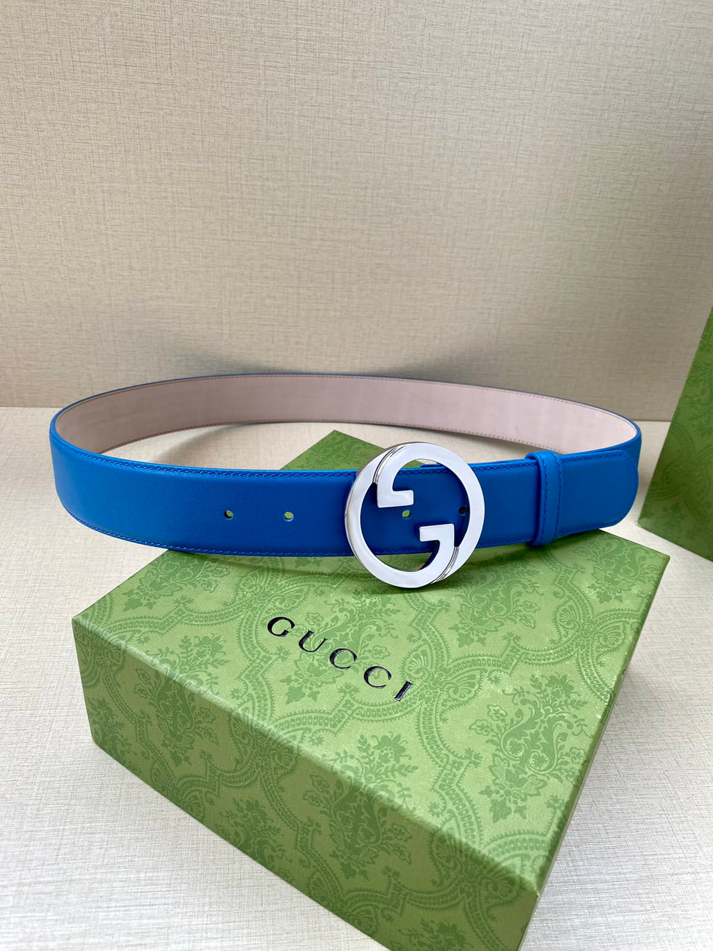 Blue Gucci belt with silver-tone circular GG buckle, flat lay, center holes visible.