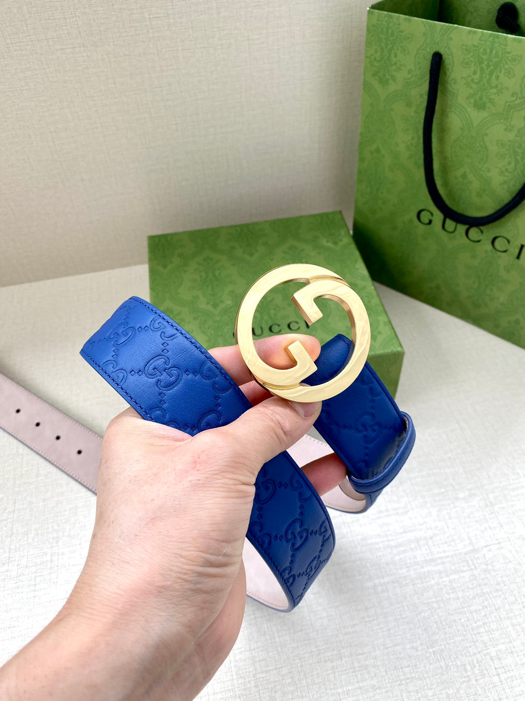 Gucci belt blue leather with gold-tone interlocking GG buckle and embossed logo pattern.