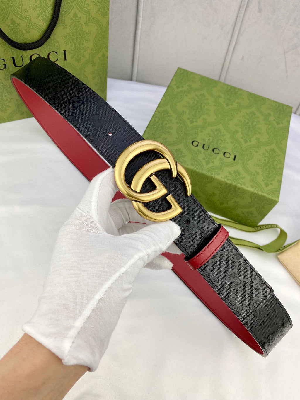 Gucci belt shown in hand: black monogram strap with red edge and gold-tone double G buckle