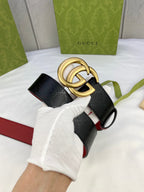 Gucci belt in hand with black monogram pattern, red inner edge, and gold-tone double G buckle