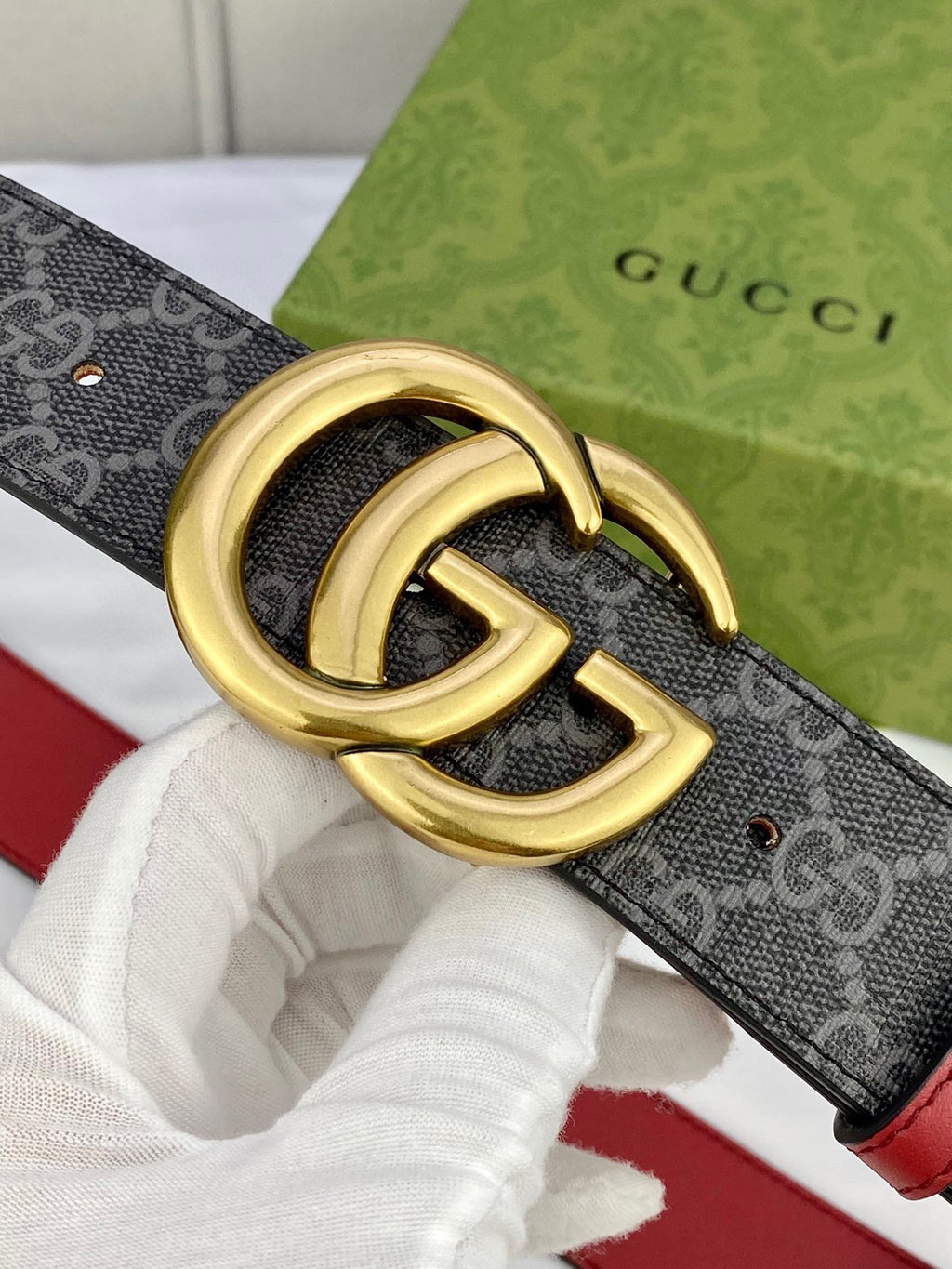 Gucci belt buckle close-up: gold double-G on dark GG-pattern strap with red edge