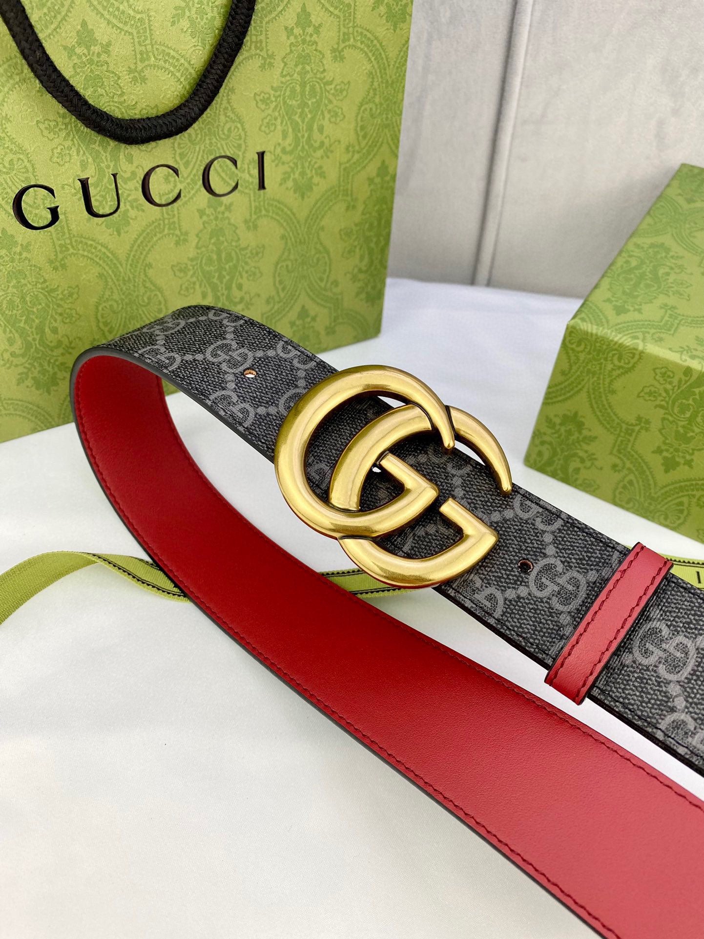 Gucci belt angled: dark GG-pattern strap, red leather sides, gold double-G buckle