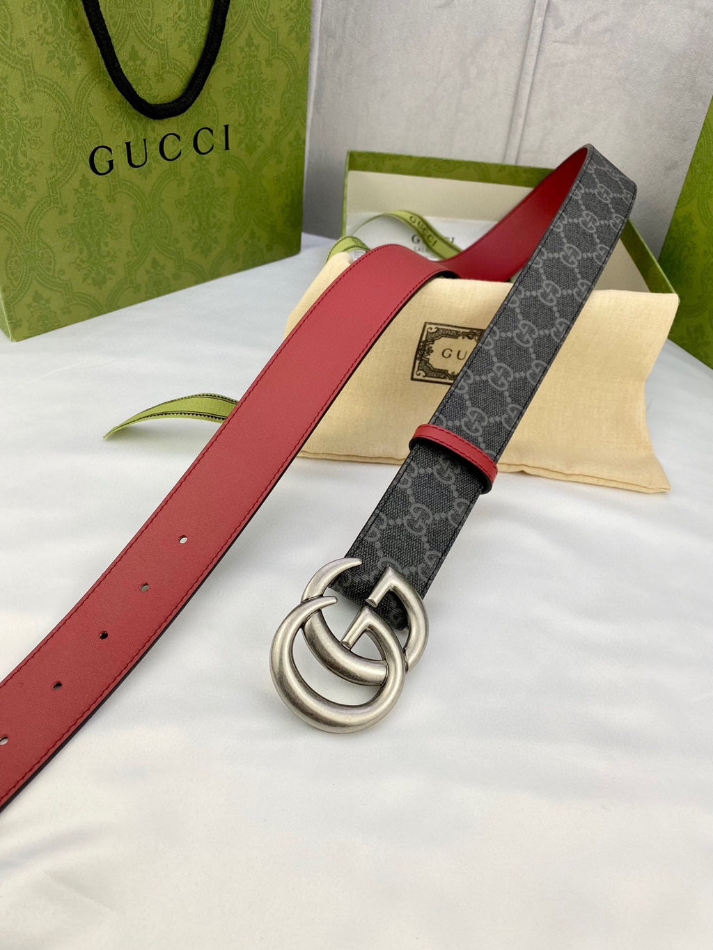 Gucci belt laid flat: dark GG-pattern strap, red leather sides, silver double-G buckle