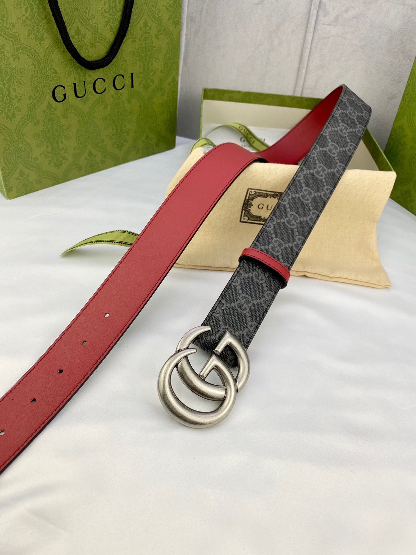 Gucci belt laid flat: dark GG-pattern strap, red leather sides, silver double-G buckle