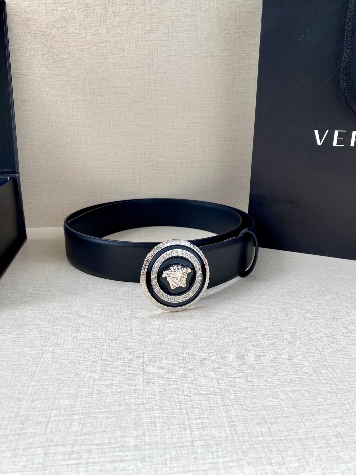 Dark blue Versace belt with round Medusa buckle, displayed beside shopping bag