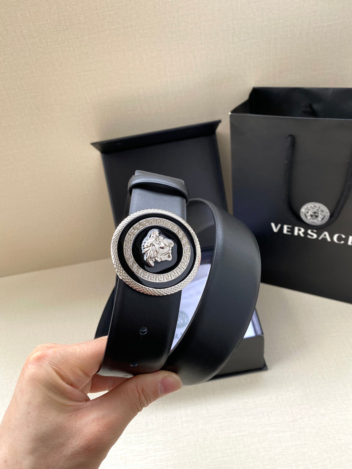 Versace dark blue belt, close-up of round Medusa buckle on curved strap