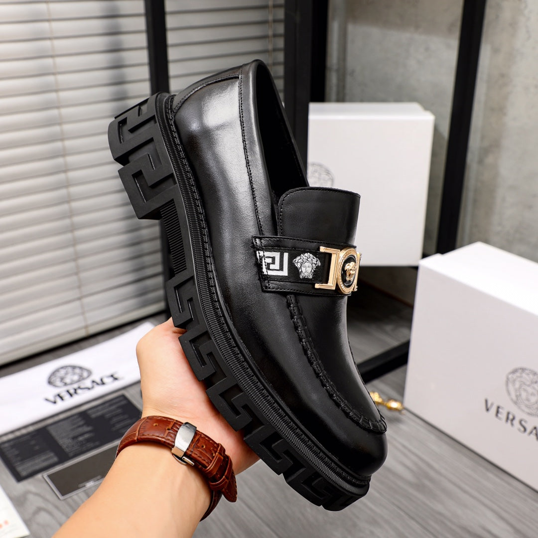 Black leather loafer with gold buckle emblem and chunky tread outsole, side view.