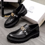 Black leather loafer pair with gold emblem buckle straps and textured lug sole.
