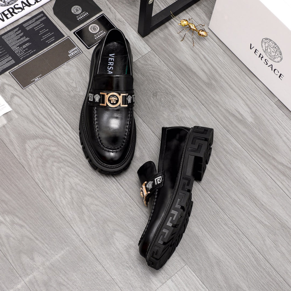 Black leather loafers with gold logo bar buckle and patterned outsole, top view pair.