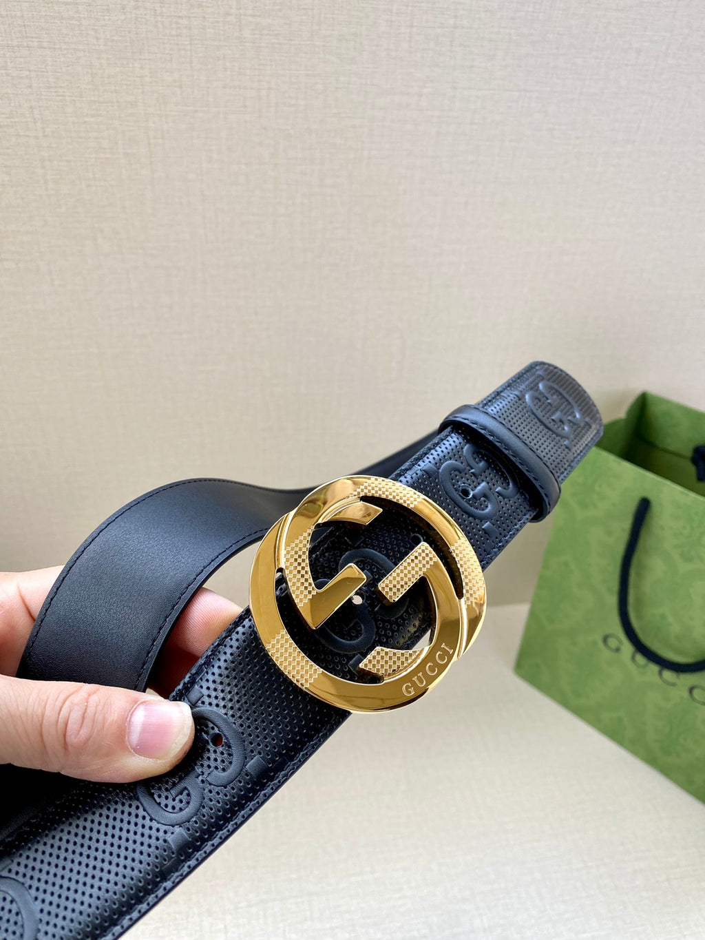 Navy leather belt with embossed logo pattern and gold-toned buckle close-up