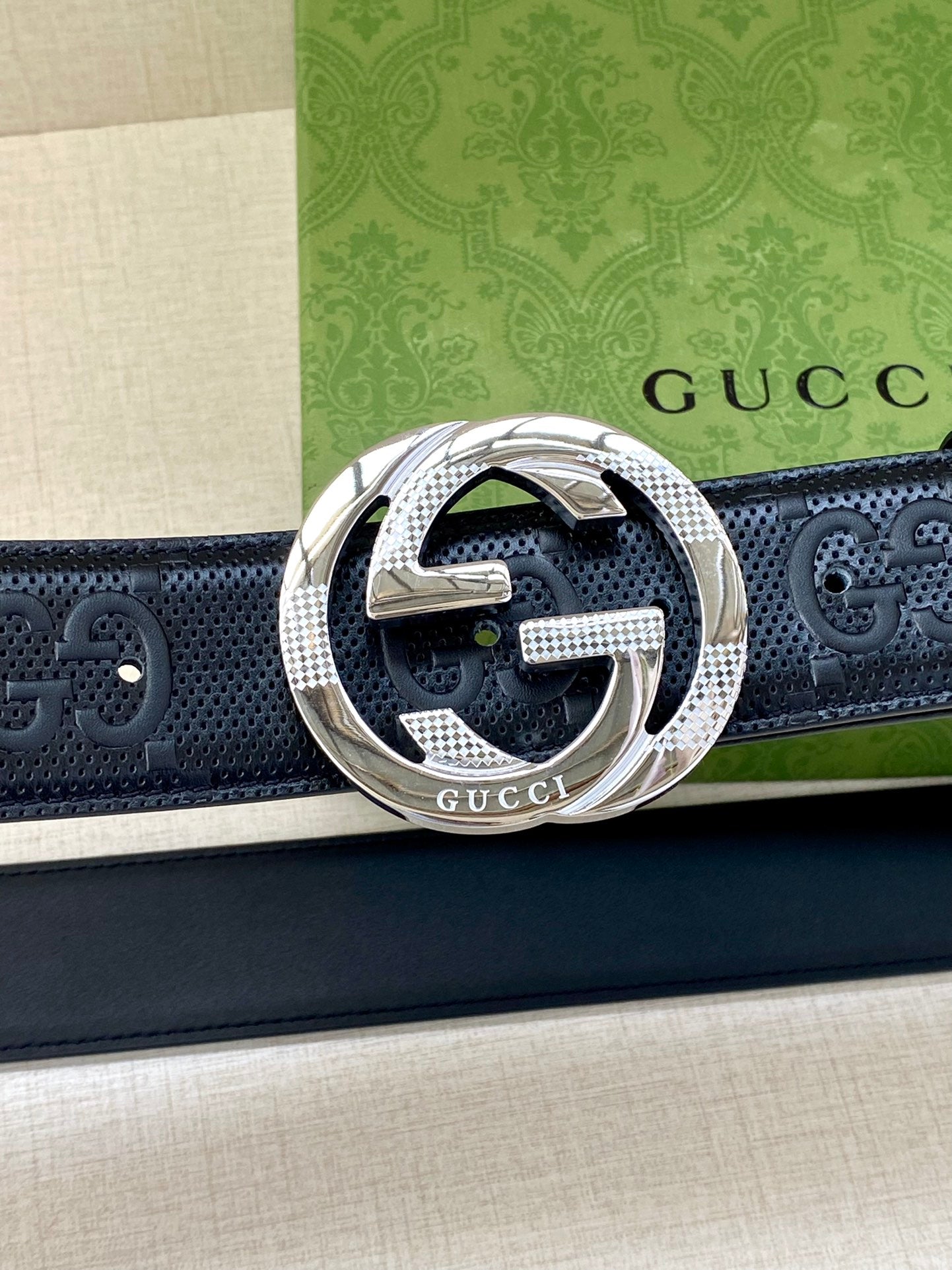 Dark leather belt with perforated logo texture and silver-toned interlocking G buckle