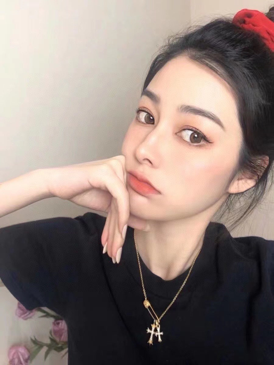 Gold cross pendant necklace worn by person with black top