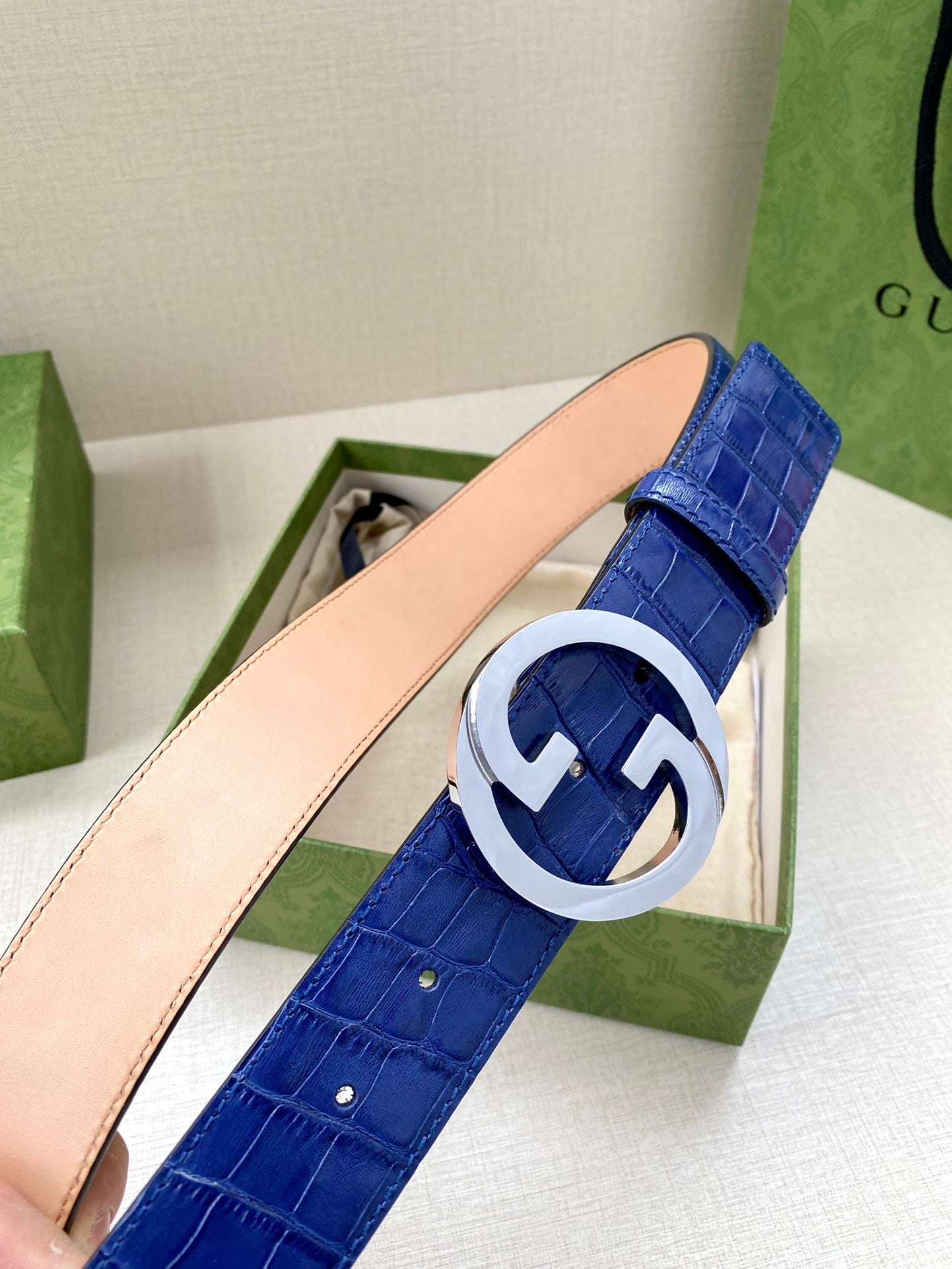 Blue croc-embossed Gucci belt with white metal GG buckle close-up