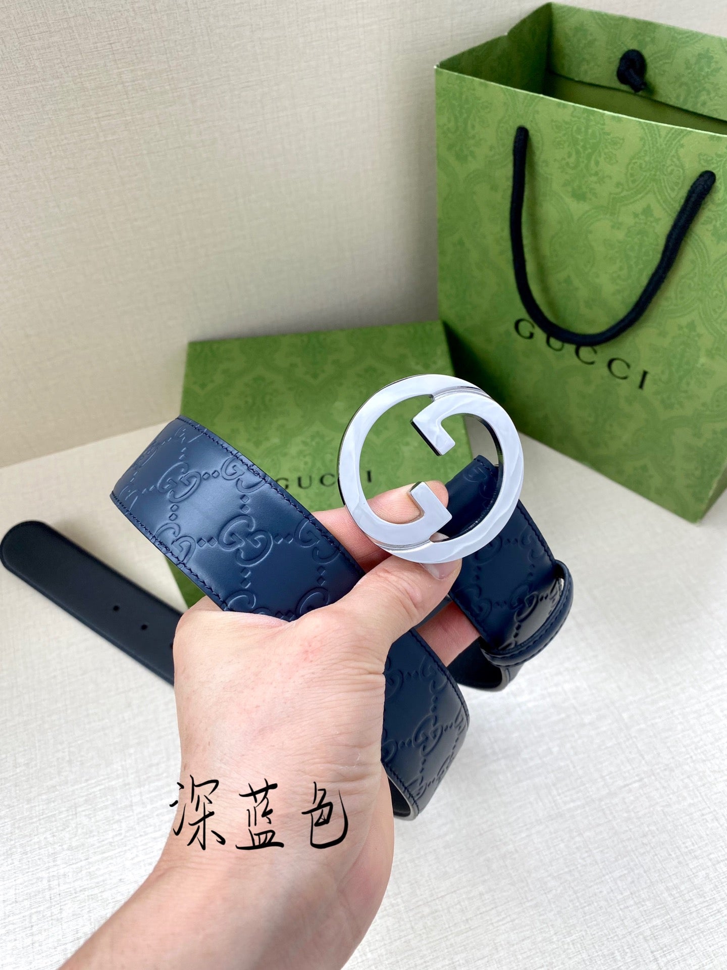 Gucci belt close-up: dark blue strap with white-ring G buckle, held up