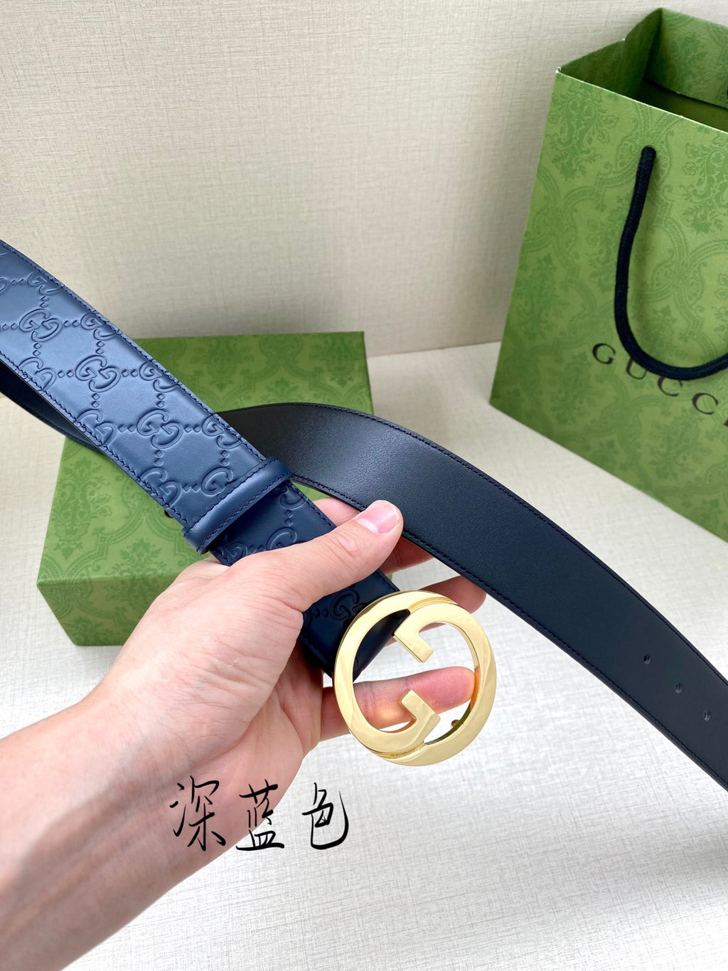 Gucci belt close-up: dark blue strap and gold G buckle in hand