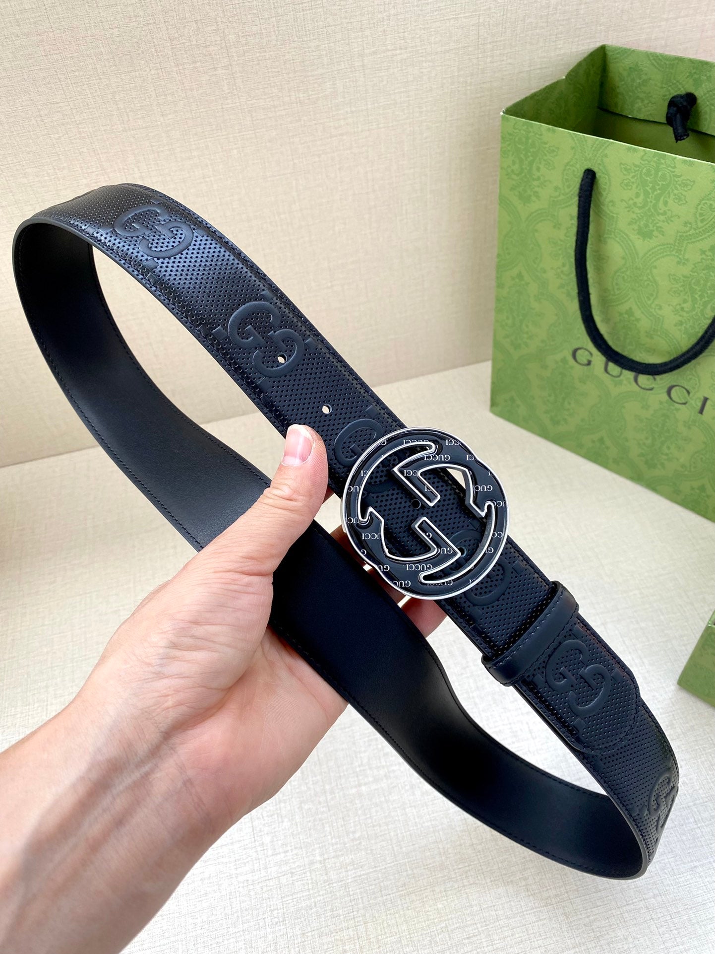 Gucci dark navy belt held in hand, featuring GG-pattern strap and oval buckle