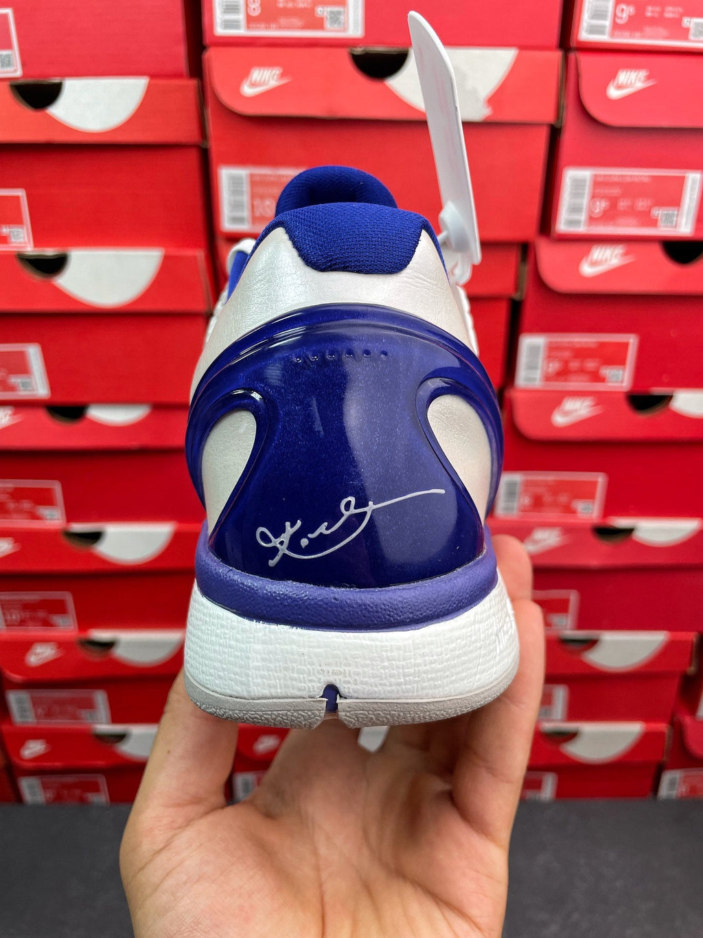 Blue and white basketball sneaker heel view with swoosh graphic and lace tag.