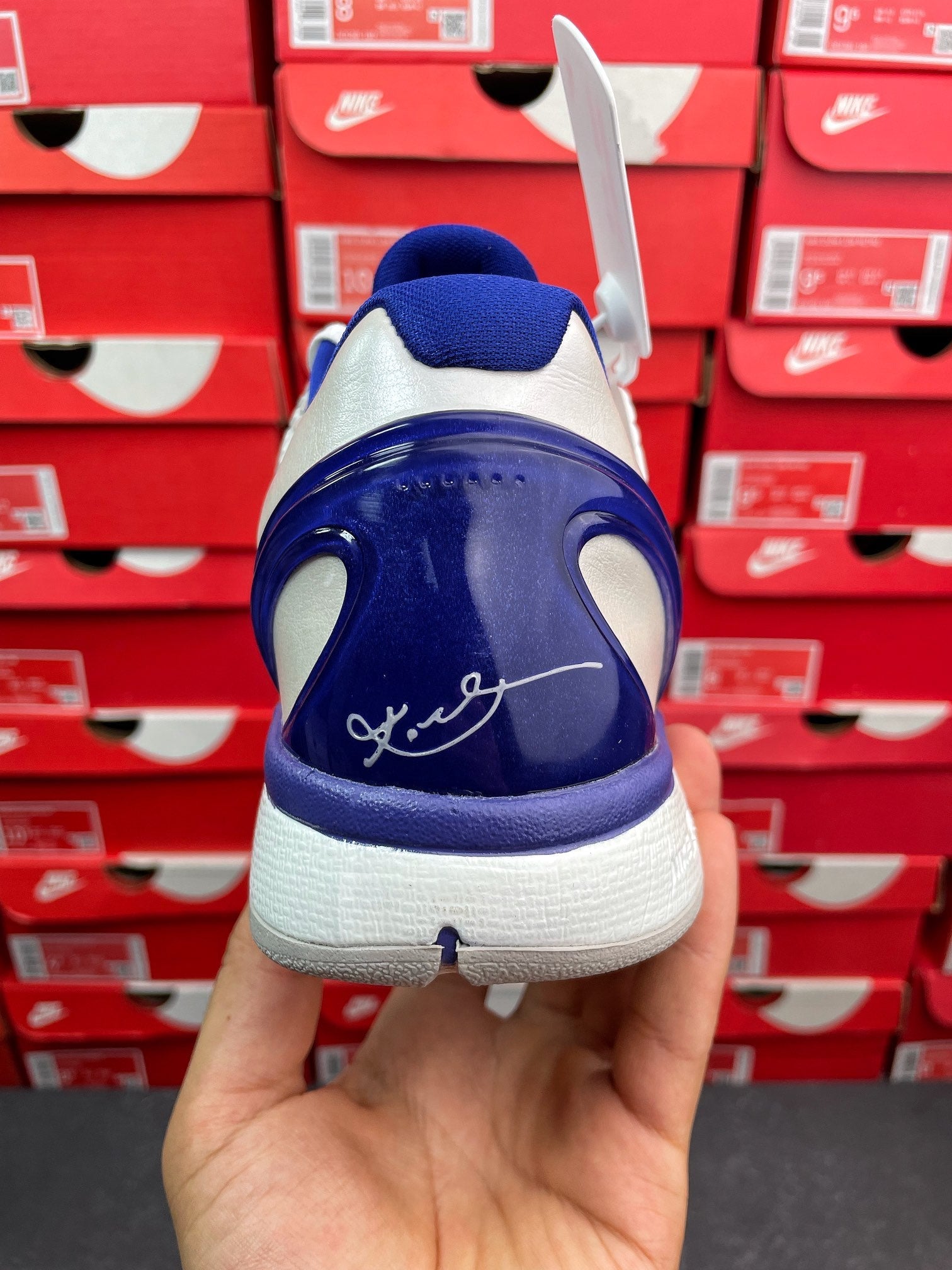 Blue and white basketball sneaker heel view with swoosh graphic and lace tag.